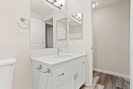 A white bathroom with a sink, mirror, and toilet.