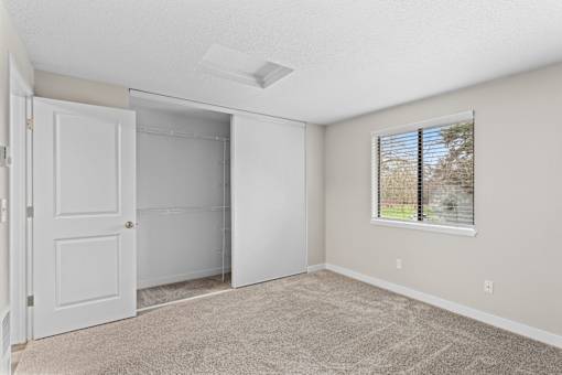 A room with a white door, a window with blinds, and a carpeted floor.