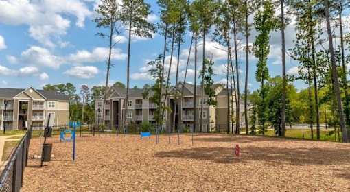 A playground with a sandy area and a fence in front of apartment buildings.