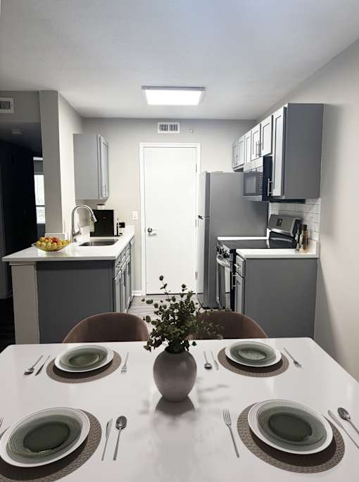 A dining table set with plates and cutlery is in the foreground of a modern kitchen.