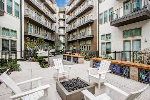 A patio area with white chairs and tables in front of apartment buildings.