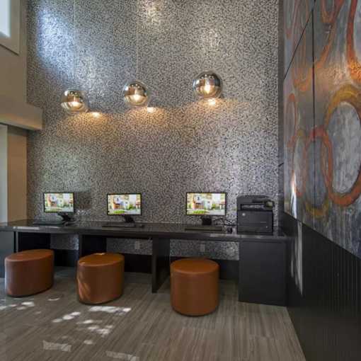 A modern office space with a grey floor, a grey wall with a circular design, and three computers on a desk.