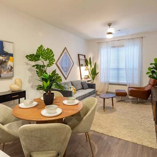 A living room with a round table and chairs, a sofa, and a potted plant.