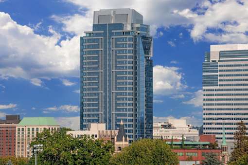 A tall building with a glass facade stands in front of a sky with clouds.