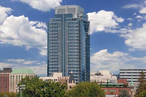 A tall building with a grey top stands in front of a sky with clouds.