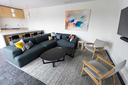 A grey couch with a yellow pillow is in the middle of a grey rug in a living room at Brookland Apartments, Oregon