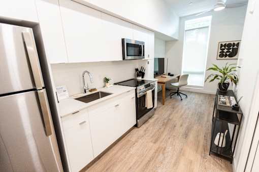A modern kitchen with a refrigerator on the left and a dining area with a chair and a table at Brookland Apartments, Oregon