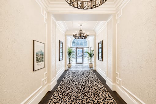A hallway with a chandelier, framed pictures, and a floral carpet.