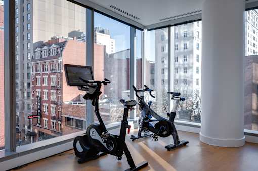Two exercise bikes are placed in front of a window with a view of the city.