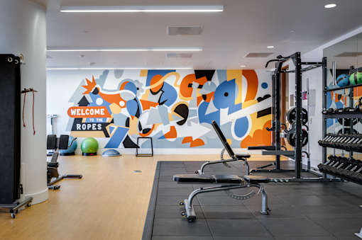 A gym with a large mural on the wall and various exercise equipment.