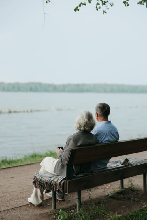 a man and woman sitting on a bench next to a lake