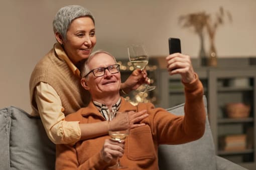 a woman and man sitting on a couch holding wine glasses and looking at a cell phone