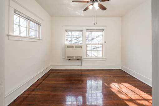 A room with a ceiling fan and two windows.