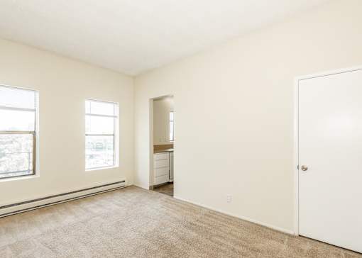 A room with a carpeted floor, a white door, and a window with a view of trees.