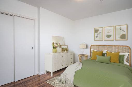 A bedroom with a bed, nightstand, and a plant on the nightstand.
