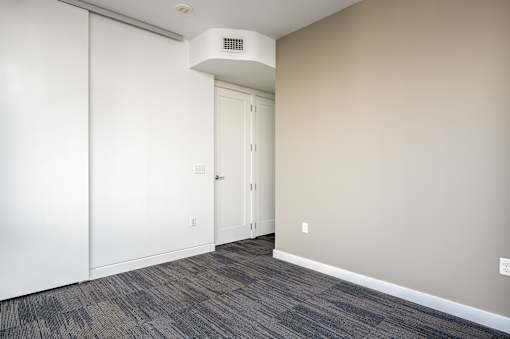 A room with a white door and a grey carpet.