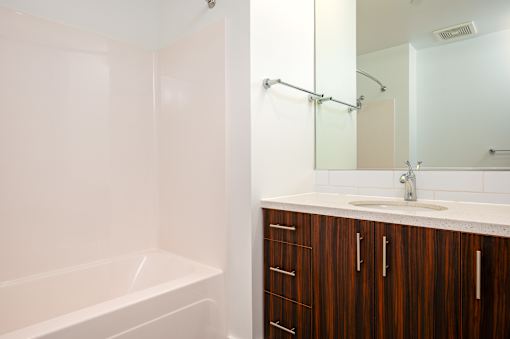 A white bathroom with a wooden cabinet and a white tub.