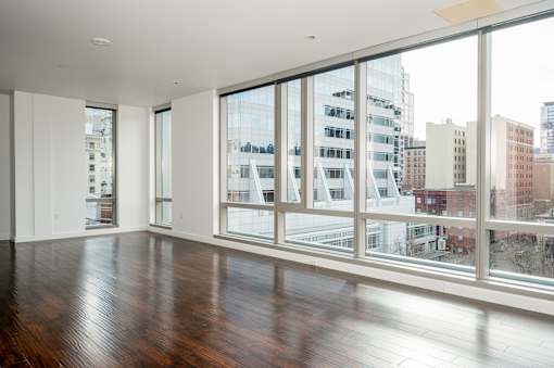 A large empty room with wooden floors and large windows overlooking a cityscape.
