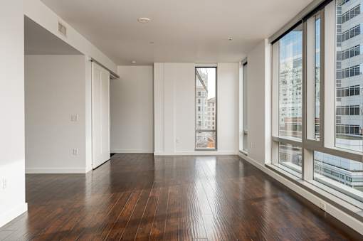 A large empty room with wooden floors and a view of a cityscape through the windows.