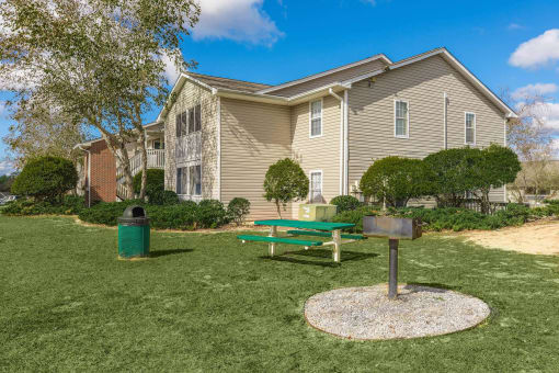 a picnic table and grill sit in a grassy area in front of an apartment building