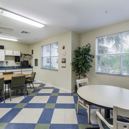 a room with a table and chairs and a kitchenette in the background