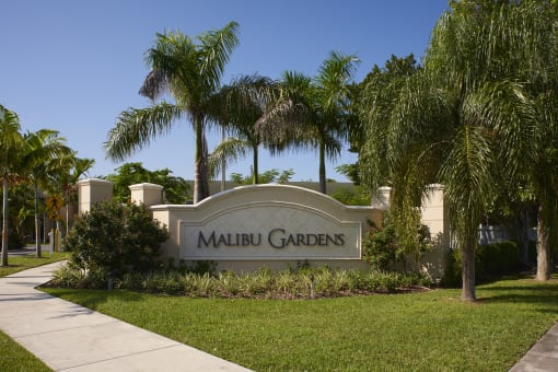 a sign gardens in front of palm trees