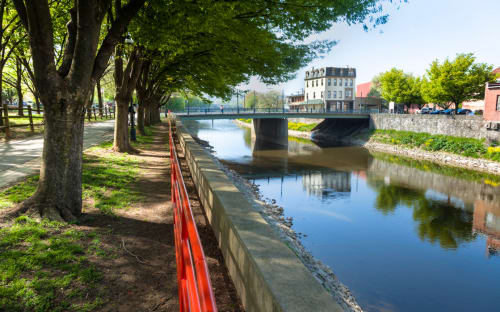 a path next to a river with trees and a bridge