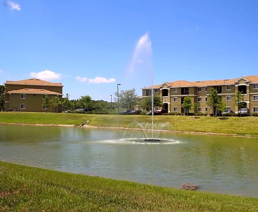 a fountain in the middle of a lake with apartment buildings in the background