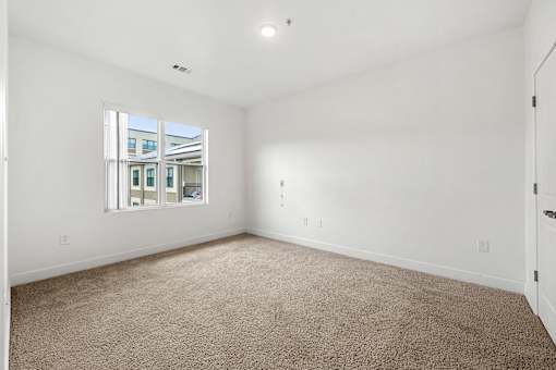 A large empty room with a carpeted floor and a window.