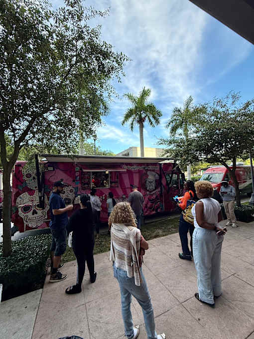 A group of people are standing in front of a pink food truck.