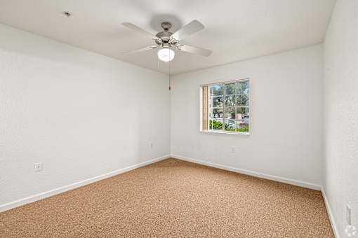 A room with a ceiling fan and a window with a view of trees and houses.