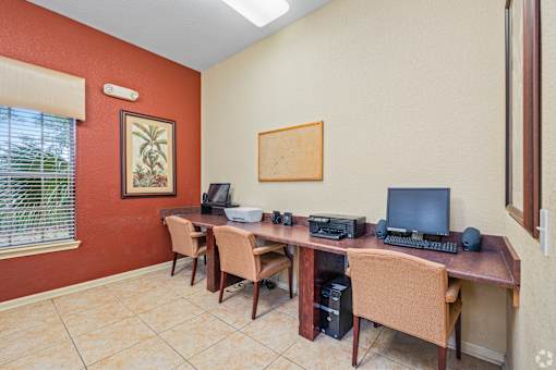 A room with a desk and chairs, a computer, and a printer.
