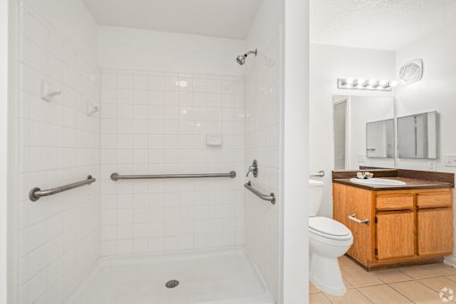 A white tiled bathroom with a wooden vanity and a walk-in shower.