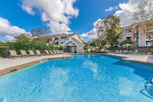 a swimming pool with chairs and umbrellas in front of a house at Arbors at Windsor Lake, Columbia, SC  