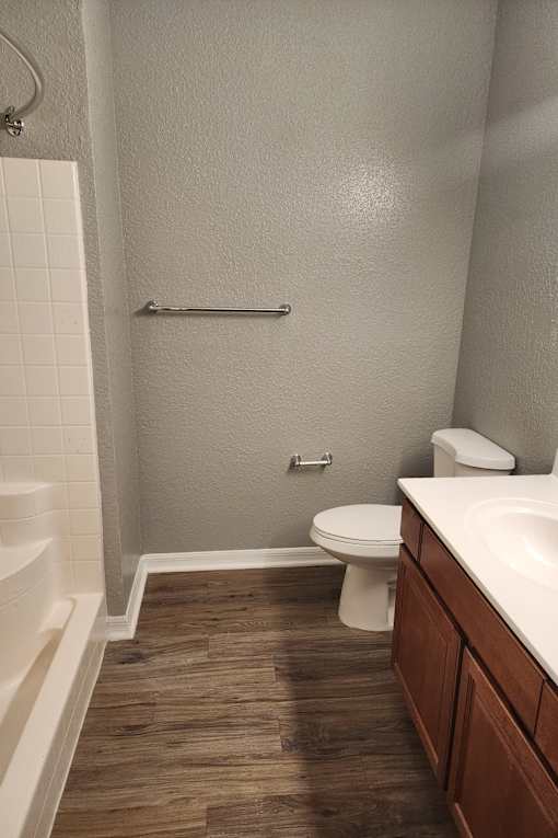A white toilet sits in a bathroom with wood flooring and white walls.