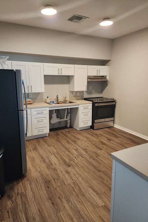 A kitchen with a black fridge, white cabinets, and a wooden floor.