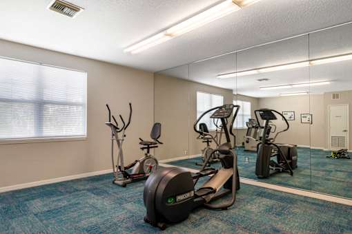 A gym with a variety of exercise equipment including treadmills, stationary bikes, and elliptical machines.