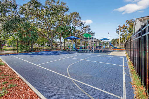 A basketball court is surrounded by a fence and trees.