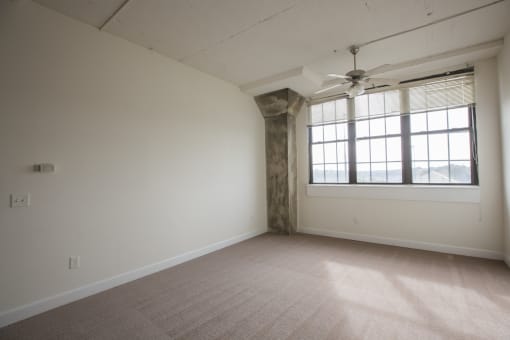 an empty bedroom with a large window and a ceiling fan