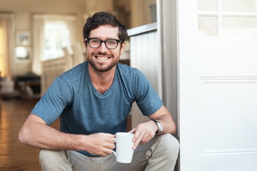 a man sitting on a door holding a coffee cup