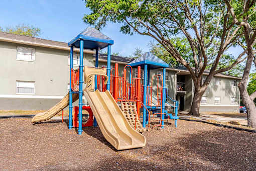 A playground with a blue and orange slide in front of a building.