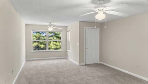 an empty living room with a ceiling fan and a window