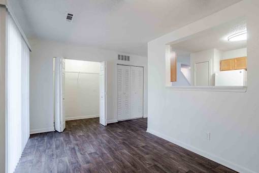 A room with white walls and wooden flooring with a mirror on the wall.