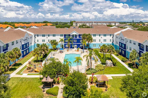 A large swimming pool is surrounded by palm trees and a resort-style building.