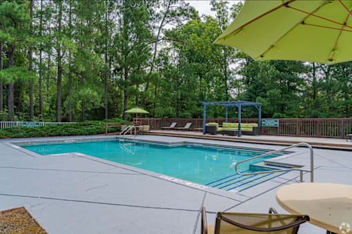 A pool surrounded by trees and a yellow umbrella.