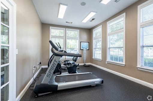 A treadmill in a room with a TV and windows.