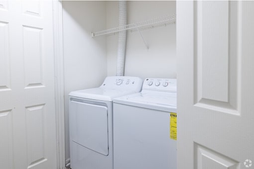A white dryer is in a small room with a white door on the left and a white door on the right.