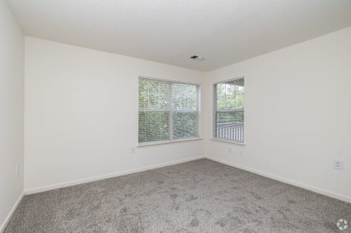 A room with a carpeted floor and two windows.