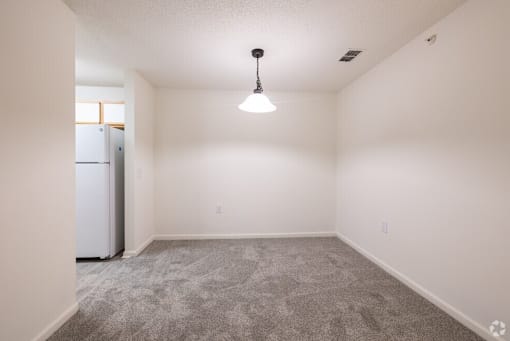 A room with a grey carpet and a white fridge.