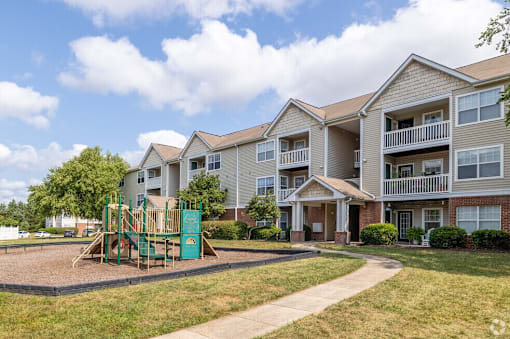 A playground with a green slide is in front of apartment buildings.